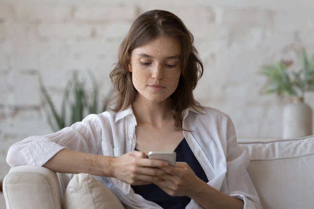 istock Young woman use cellphone sit on couch at home 1424679252