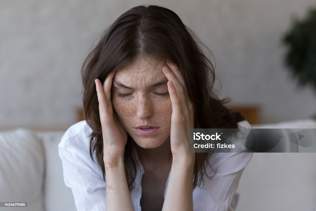 Freckled woman touches temples suffers from headache feels unhealthy, closeup Young freckled woman closed eyes, touches her temples suffers from severe headache feels unhealthy, close up face shot. Life troubles, panic attack, painful sensations, chronic migraine hurt concept Headache Stock Photo