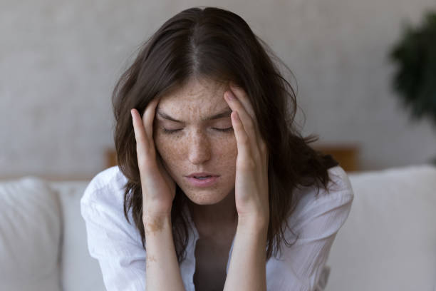 Freckled woman touches temples suffers from headache feels unhealthy, closeup stock photo