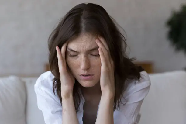 Photo of Freckled woman touches temples suffers from headache feels unhealthy, closeup