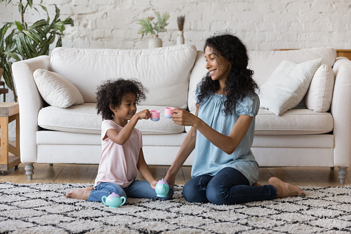 African mother and daughter holds toy tea cups playing indoor
