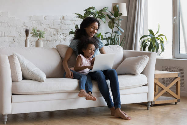 istock Smiling African mom and daughter sit on sofa use laptop 1424679810