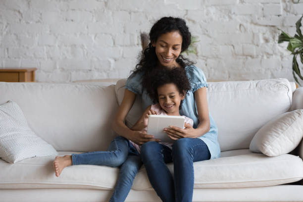 istock African mother her daughter sit on sofa using digital tablet 1424679816