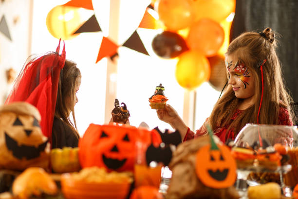 Two little girls cheering with cupcakes during a Halloween party stock photo