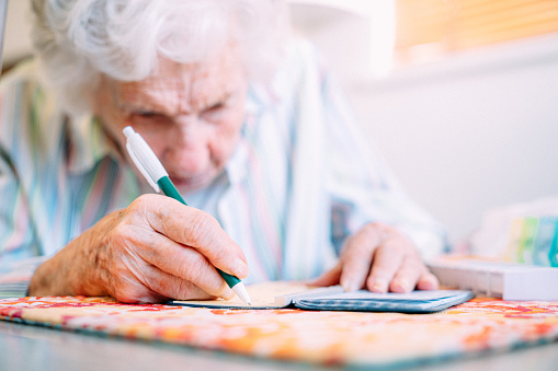 Ultra Close-Up Shot of an Elderly Senior Caucasian Woman's Hands As She Looks Close and Using a Pen to Write a Check