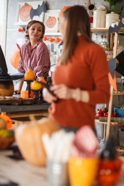 istock Young woman looking over shoulder, smiling at her mother while decorating for Halloween 1424692100