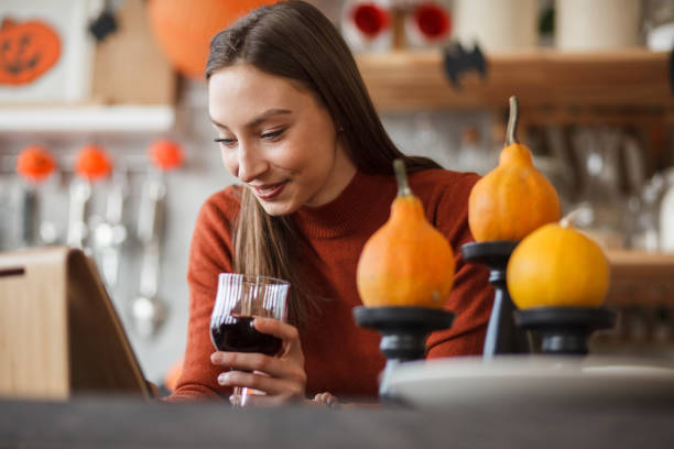 ワインを飲みながらデジタルタブレットを使用する若い女性 - glass autumn halloween food ストックフォトと画像