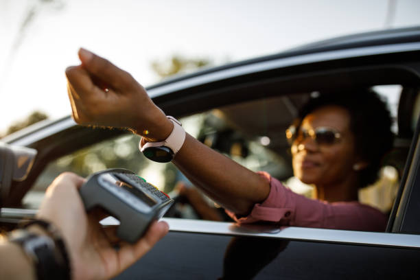Selective focus shot of woman using smart watch to pay for drive through order Low angle view of woman holding her smart watch over a payment terminal when paying for her order at the drive through. curbsidepickup stock pictures, royalty-free photos & images