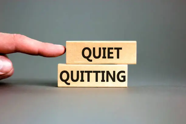 Photo of Quiet quitting symbol. Concept words Quiet quitting on wooden blocks. Beautiful grey table grey background. Businessman hand. Business and quiet quitting concept. Copy space.