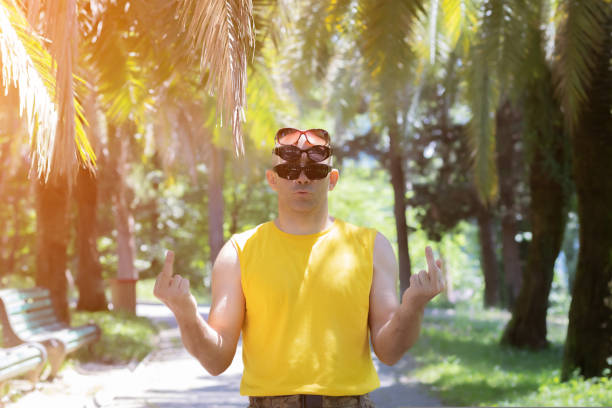 istock A man shows a gesture with two hands fuck you. Three glasses on his head 1424702959