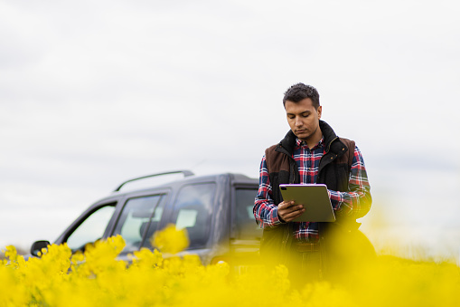 Modern agriculture.  Young and attractive Middle Eastern farmer holding a tablet in a field with an off-road SUV in the background . Modern technology in agriculture. Modern farming. Modern farming technology.