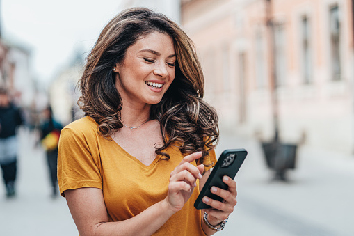 Cheerful young woman texting outdoor in the city. Happy woman using smartphone on the street. Happy to be Connected always and everywhere,