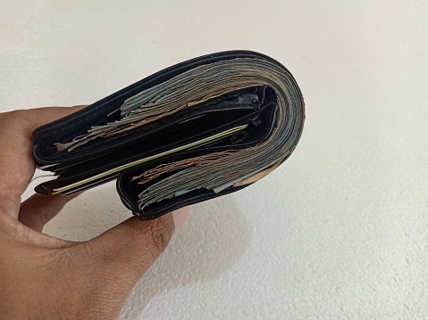 someone folds a leather wallet that contains a lot of rupiah, the wallet is difficult to fold because it is too thick. Photo illustration of having a lot of money after receiving a bonus from work. isolated on white