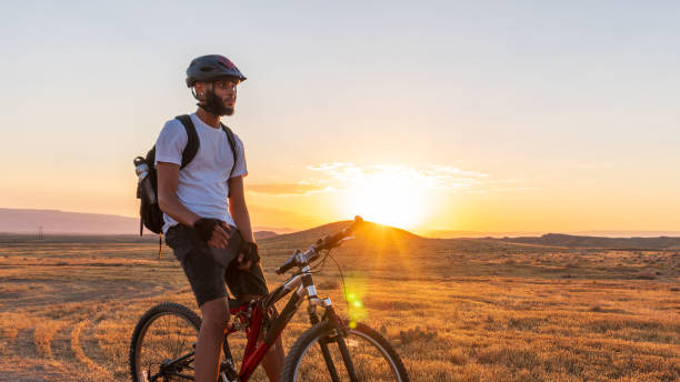 산악 자전거에 앉아있는 동안 해질녘에 들판을 바라 보는 젊은 아프리카 계 미국인 남자 - mountain biking cycling action bicycle 뉴스 사진 이미지