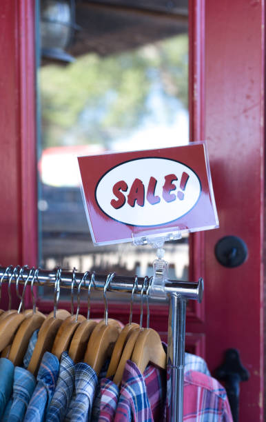 Red Sign on Outdoor Clothing Rack: "SALE!" Red Sign on Outdoor Clothing Rack: "SALE!" Shot in Taos, NM. colorful check shirts on sale at a clothing store stock pictures, royalty-free photos & images