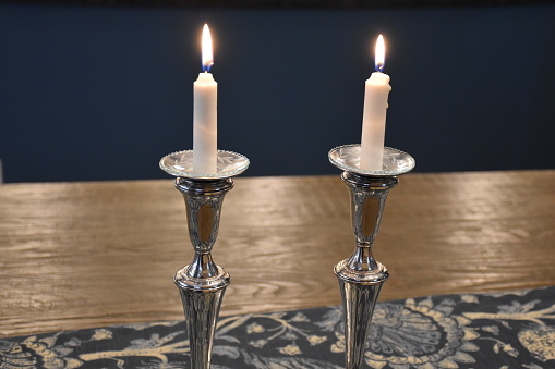 2 lit shabbat candles on blue cloth a d wooden table