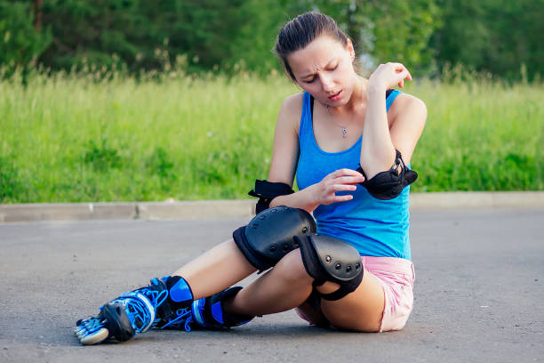 attractive young athletic slim brunette woman in pink shorts and blue top with protection elbow pads and knee pads on roller skates sitting on the asphalt in the park . fall concept attractive young athletic slim brunette woman in pink shorts and blue top with protection elbow pads and knee pads on roller skates sitting on the asphalt in the park . fall concept elbow pad stock pictures, royalty-free photos & images