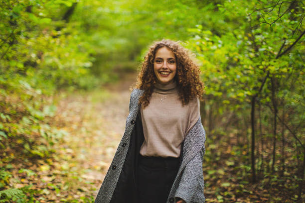 Redhead curly beautiful girl in coat in autumn forest. Pretty woman enjoying vacation. Visit local attractions. Girl laughing in nature. Feel happiness. Charming smile. Happy lady stock photo