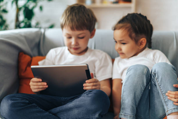 Children sitting on the couch watching videos on the tablet stock photo
