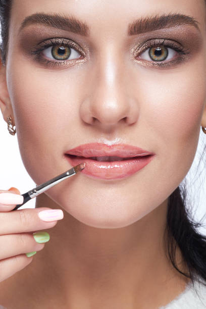 istock Female paint her lips by cosmetic brush lipstick on lips 1424764929