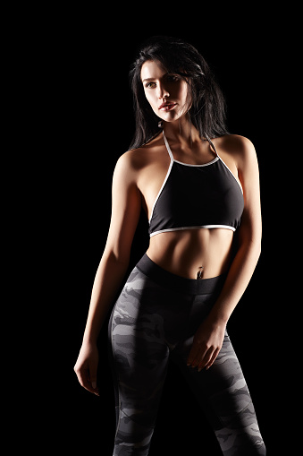 Portrait of a young brunette sporty fitness woman on black background