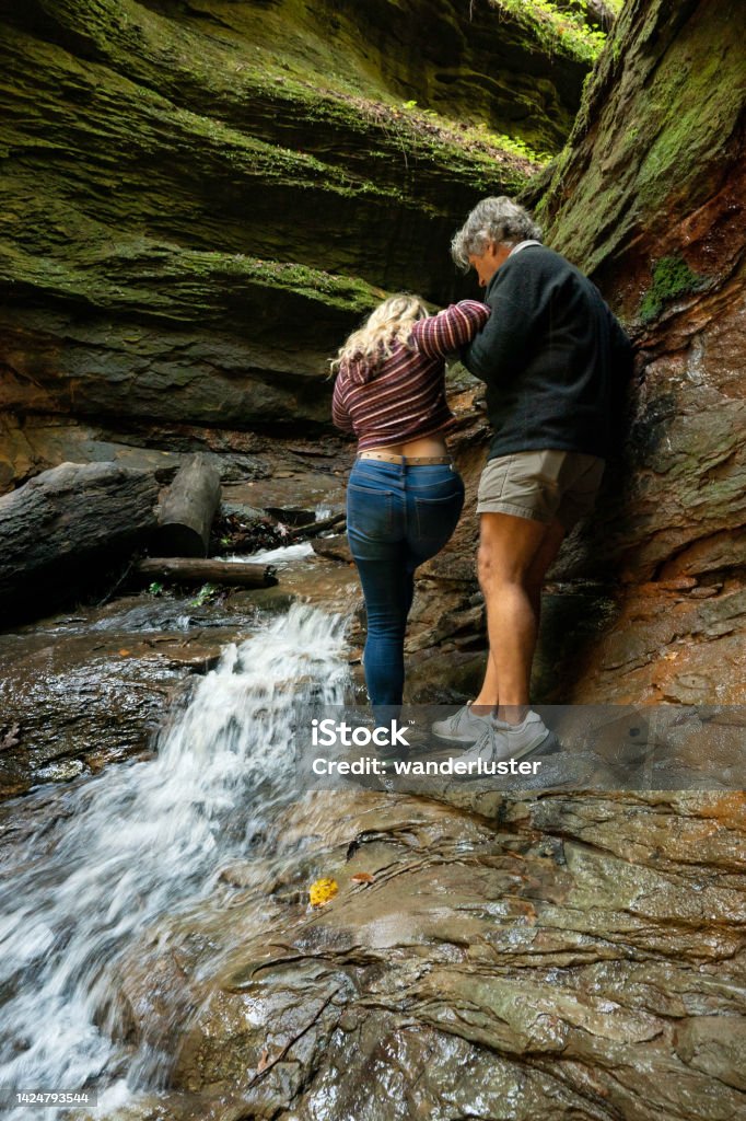 Slippery hiking at Turkey Run State Park, Indiana Father helps his college age daughter across slippery rocks in a waterfall canyon while hiking at Turkey Run State Park, Indiana Autumn Stock Photo