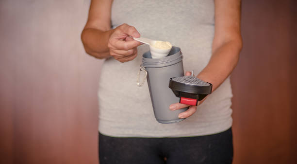 istock Woman pouring protein powder into protein blender 1424796709