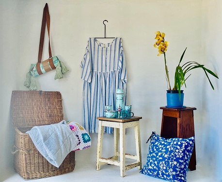 Horizontal still life of rustic country store display with orchard pillow linen basket dress tea set on distressed wood stool and beach towel in holder against white wall in Newrybar Australia