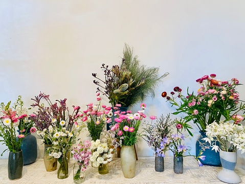 Horizontal still life of ceramic vases holding bunches of bright spring bloom flowers against white wall