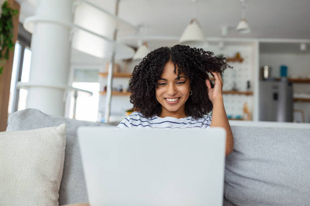 istock Attractive young woman sitting alone on her sofa at home and using her laptop 1424809251