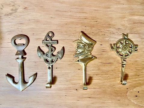 Horizontal still life of 4 brass hooks with ocean sailing theme design in a row on wood table for hanging items on interior wall