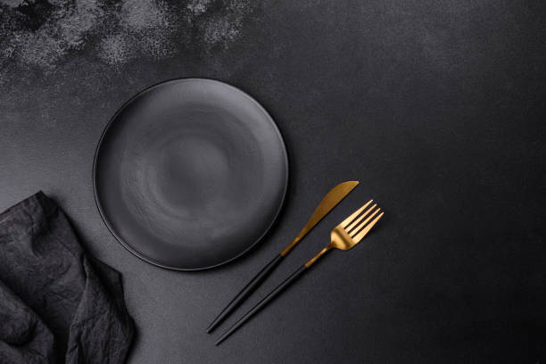 istock An empty black plate on a dark concrete background with spices, herbs and cutlery 1424814910