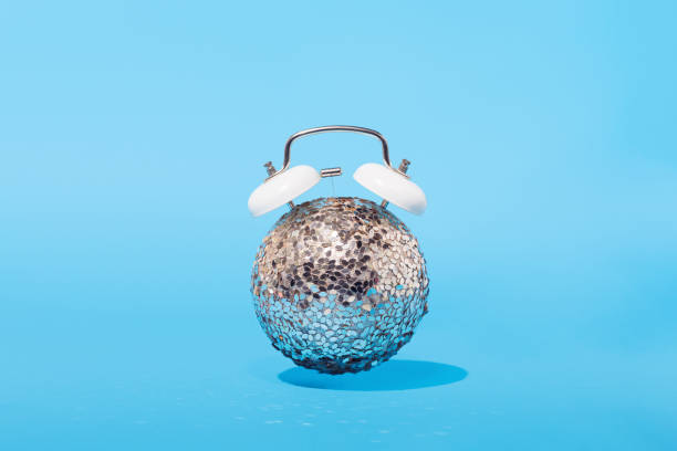 idea conceptual de navidad: reloj despertador con brillante bola de año nuevo sobre fondo azul. concepto de naturaleza muerta mínima - clock face flash fotografías e imágenes de stock