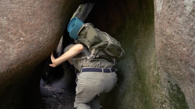 A mature male adventurer with hiking equipment exploring a forest cave