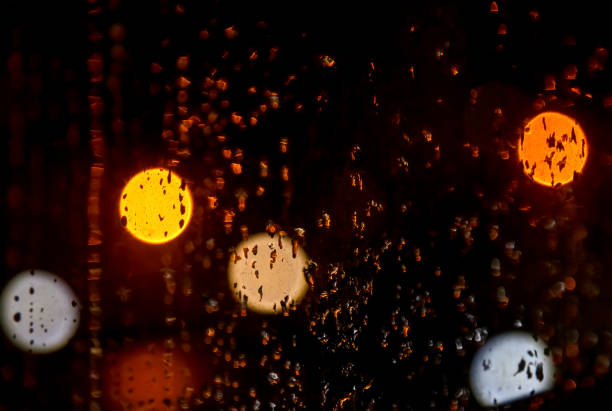 Rain drops on glass for backgrounds rainy fall autumn weather. Night abstract background with raindrops on window and blurred light. Outside window is blurred bokeh lamps of night city. Copy space