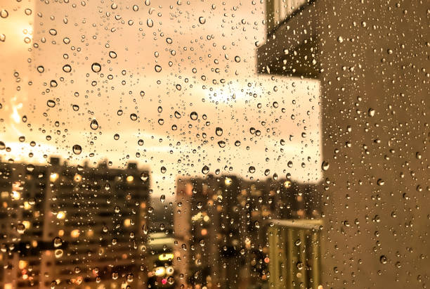 istock Rain drops on window glass for backgrounds rainy fall autumn weather. Abstract yellow background with raindrops on blurred daylight. Outside urban window is blurred bokeh water. Copy text space 1424817520