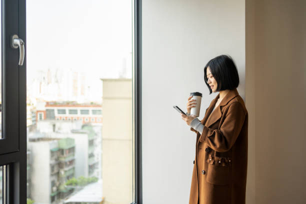 istock Asian businesswoman using smart phone by the window 1424822940