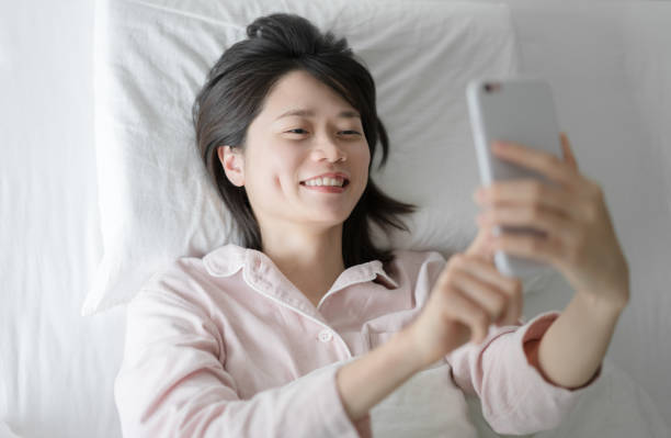 istock woman lying in white bed using smartphone gadget have video call 1424823279