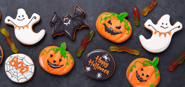 Happy Halloween. Sweets for party. Gingerbread cookies and gummy worms on a dark table. Top view stock photo