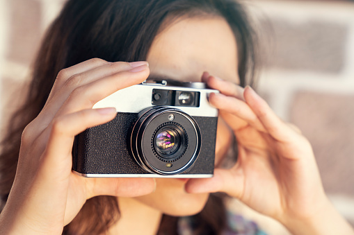 Young woman holds an analog camera and looks through the viewfinder
