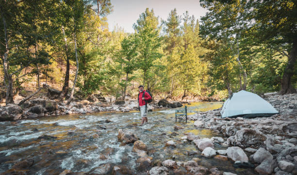 Happy male hiker camping outdoors in forest near river
