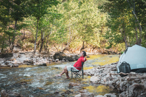 istock Man camping with feet in water by stream running through forest 1424837812