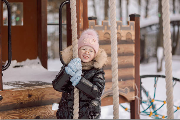 маленькая девочка гуляет на свежем воздухе зимним снежным днем в парке - playground snow winter little girls стоковые фото и изображения