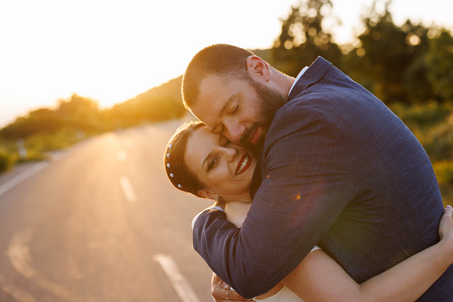 Romantic newlyweds hugging on empty road in nature at sunset