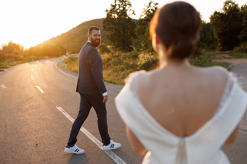 Romantic just married young couple walking on empty road in nature at sunset