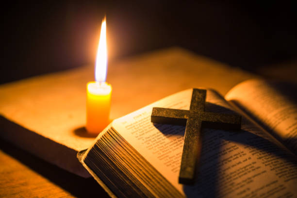 Light candle with holy bible and cross or crucifix on old wooden background in church.Candlelight and open book on vintage wood table christianity study and reading in home.Concept of christ religion encienda la vela con la santa biblia y la cruz o el crucifijo sobre el fondo de madera antigua en la iglesia. luz de las velas y libro abierto sobre mesa de madera vintage cristianismo estudio y lectura en casa. concepto de religión de cristo