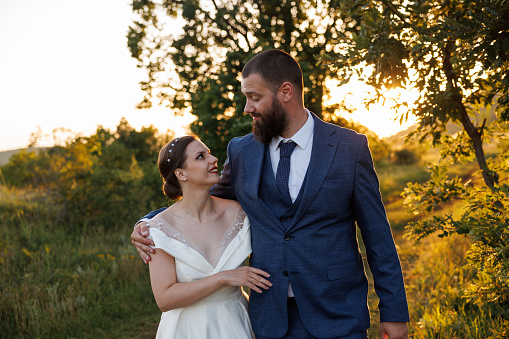 Close-up photo of a wedding couple looking at each other and walking in nature at sunset