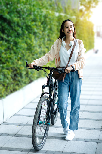 Beautiful Asian woman listening favourite music on headphones from mobile phone, Happiness relaxation summer in park with music riding bicycle in green park.