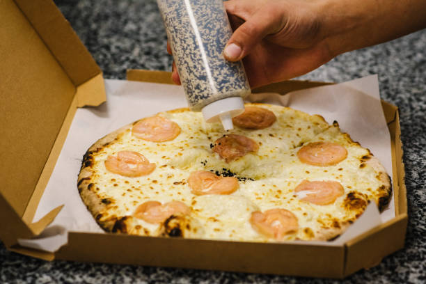 istock Chef is sprinkling white and black sesame seed over a made pizza. Baked pizza in box. Traditional Italian pizza with red salmon fish and cheese. Food delivery. Self-pickup or home delivery. Top view. 1424852673