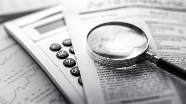Magnifying glass, calculator and charts on newspaper stock photo